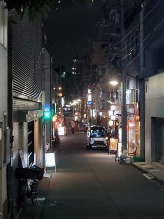 A narrow street near Shibuya, Japan. It is dark, but the street is lightly illuminated by various signs.