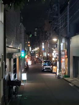 A narrow street near Shibuya, Japan. It is dark, but the street is lightly illuminated by various signs.
