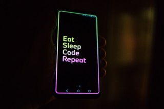 A phone with a brightly colored wallpaper that reads Eat, Sleep, Code, Repeat.
